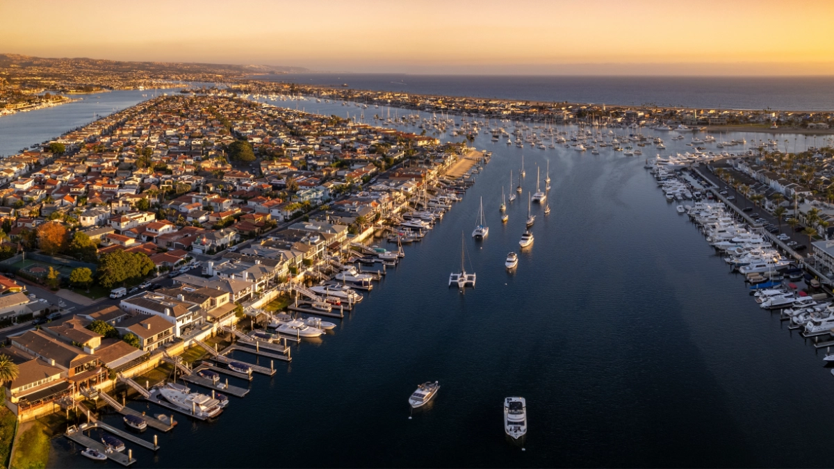 Sailboats anchored in Newport Harbor with the sun setting behind coastal homes.