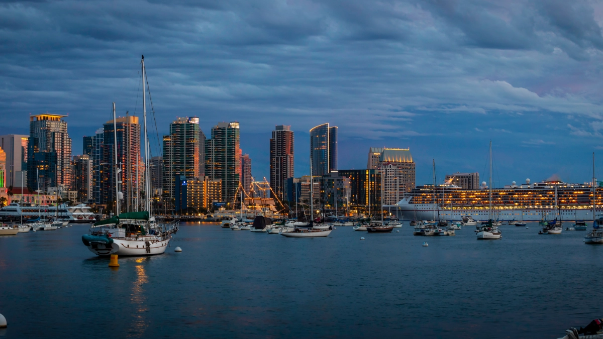 A city skyline in the evening with yachts and a cruise liner in the water.